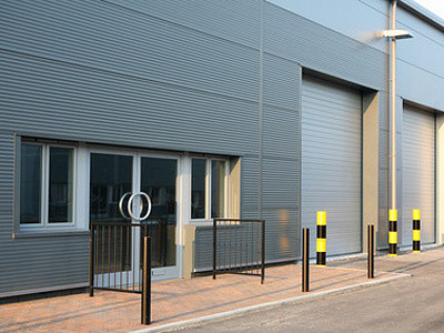 Ein graues Gebäude mit großen Rolltoren, einem Eingang und Absperrpfosten.